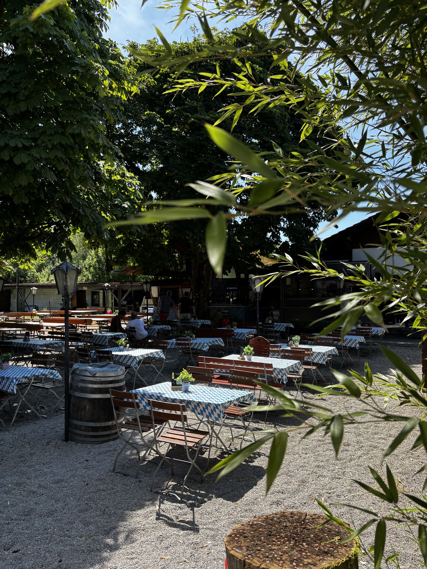Biergarten Amperwiese unter den Kastanien mit blau-weiß gedeckten Tischen, Weidenzweigen und Weinfass